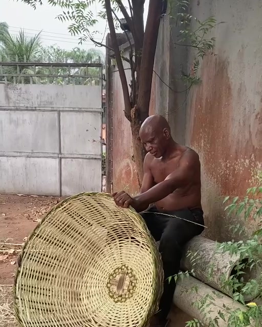 The basket maker seated beside the large woven basket he has completed